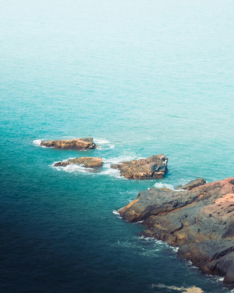 Aerial view of rocky shoreline in Gokarna, India with turquoise sea.